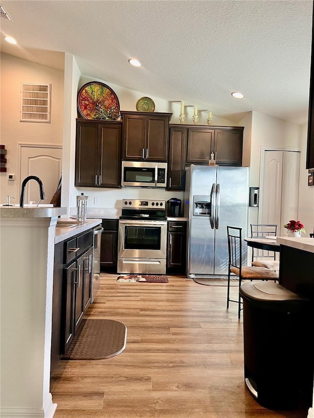 kitchen featuring dark brown cabinets, light hardwood / wood-style flooring, appliances with stainless steel finishes, and vaulted ceiling