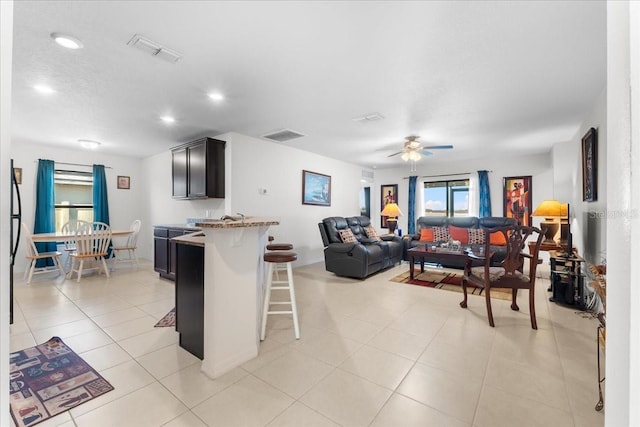 interior space with a kitchen bar, light tile patterned floors, ceiling fan, kitchen peninsula, and light stone countertops