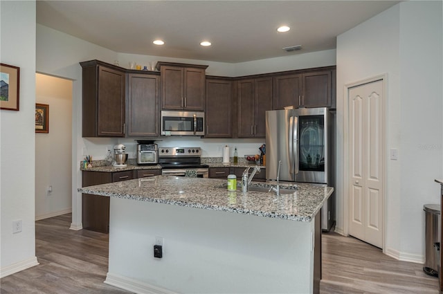 kitchen with light wood-type flooring, dark brown cabinetry, stainless steel appliances, and an island with sink