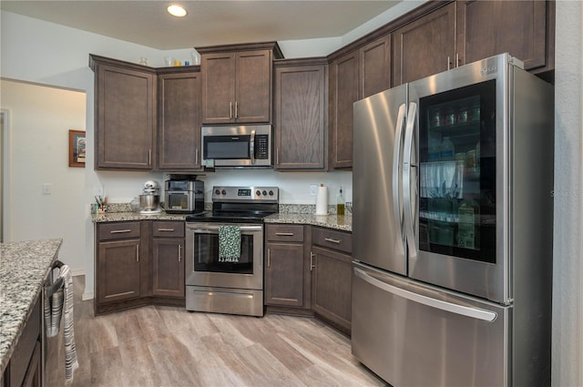 kitchen with light stone counters, light wood-type flooring, stainless steel appliances, and dark brown cabinetry