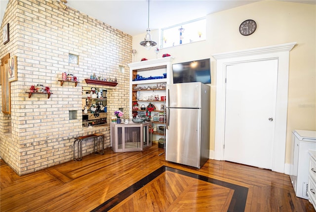 kitchen with stainless steel fridge, brick wall, hardwood / wood-style flooring, white cabinetry, and hanging light fixtures