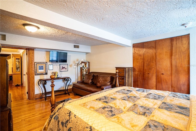 bedroom with hardwood / wood-style floors, a textured ceiling, and beamed ceiling