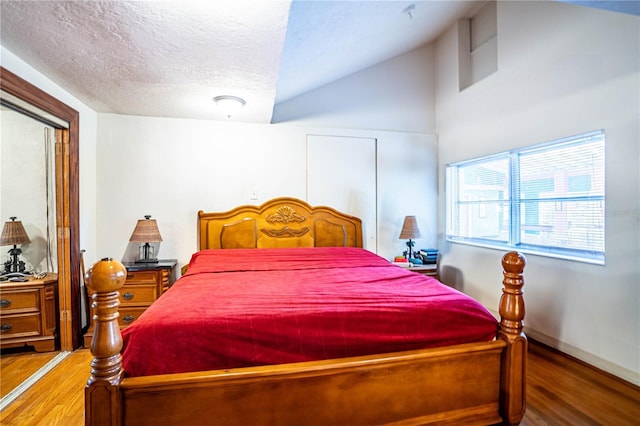 bedroom with lofted ceiling, hardwood / wood-style floors, and a textured ceiling