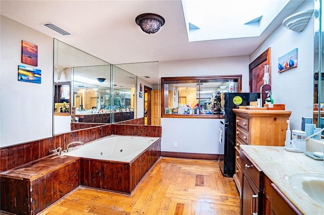 bathroom featuring vanity, parquet flooring, a washtub, and a skylight