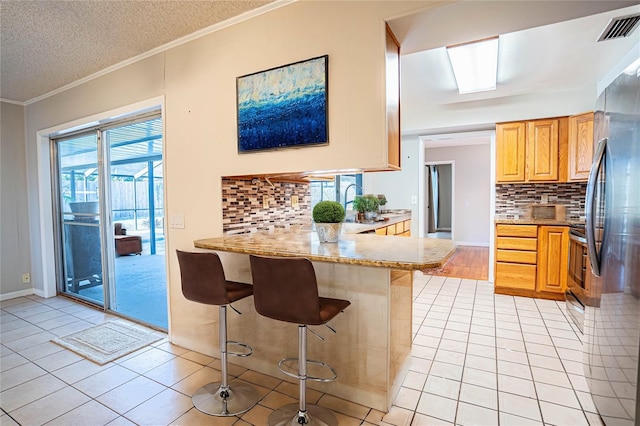 kitchen featuring a breakfast bar, kitchen peninsula, light tile patterned floors, and tasteful backsplash