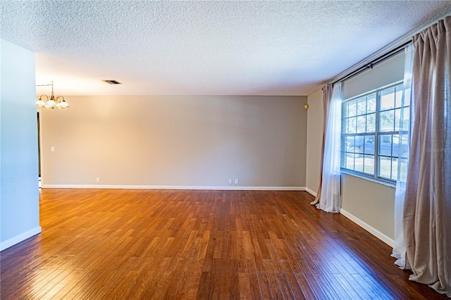 spare room featuring dark hardwood / wood-style flooring, a chandelier, and a textured ceiling