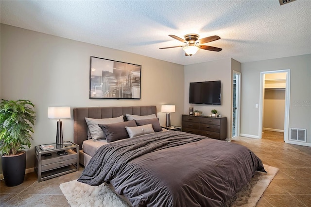 tiled bedroom featuring a textured ceiling, a walk in closet, a closet, and ceiling fan