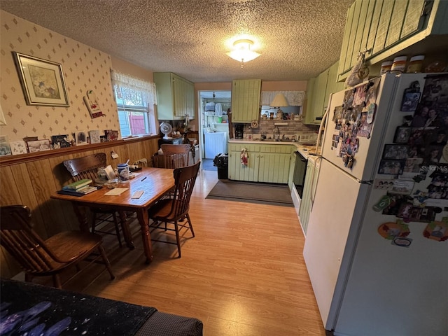 kitchen with white appliances, sink, green cabinetry, a textured ceiling, and light hardwood / wood-style floors