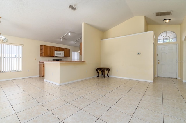 interior space featuring kitchen peninsula, light tile patterned floors, track lighting, and vaulted ceiling