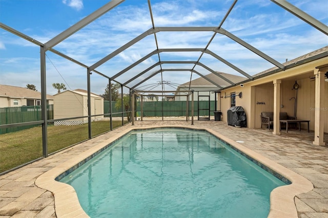 view of swimming pool featuring area for grilling, glass enclosure, a patio, a storage unit, and a lawn