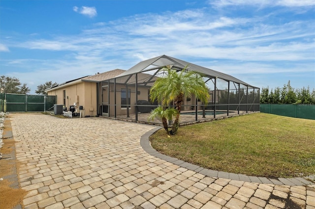 back of house featuring central air condition unit, glass enclosure, a patio area, and a lawn