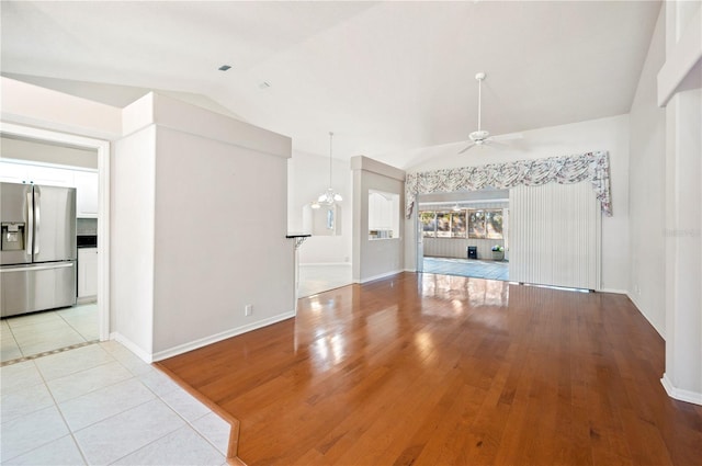 unfurnished living room featuring ceiling fan with notable chandelier, light tile patterned floors, and vaulted ceiling