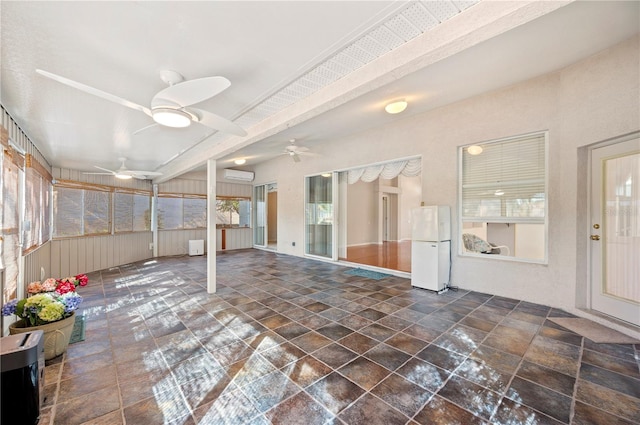 unfurnished sunroom with ceiling fan, a wall unit AC, and a wealth of natural light