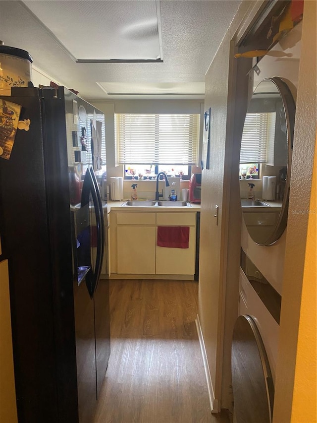 kitchen with sink, light hardwood / wood-style flooring, a textured ceiling, black fridge with ice dispenser, and stacked washer / dryer