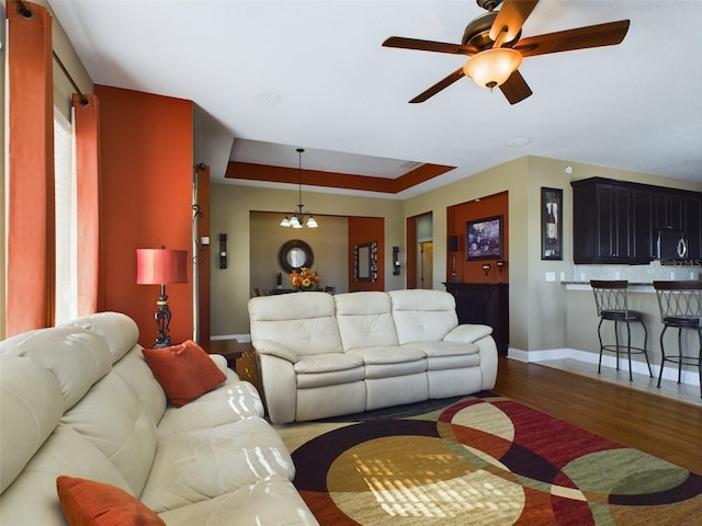 living room featuring ceiling fan with notable chandelier, wood-type flooring, and a tray ceiling