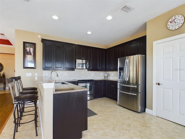 kitchen with stainless steel appliances, a kitchen breakfast bar, light stone counters, decorative backsplash, and light tile patterned floors