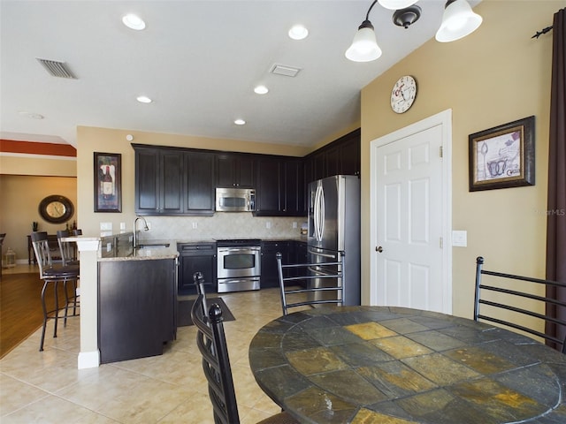 kitchen featuring tasteful backsplash, stainless steel appliances, sink, light tile patterned floors, and hanging light fixtures