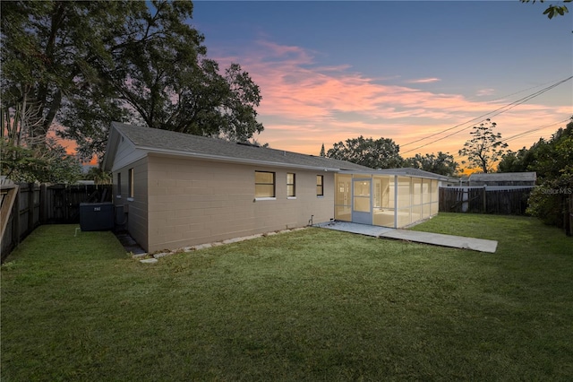 back house at dusk featuring a sunroom and a yard