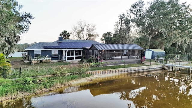 1769 S Lake Reedy Blvd, Frostproof, FL 33843 - back of house featuring a sunroom, a shed, roof mounted solar panels, a chimney, and a water view