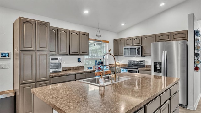 kitchen featuring dark brown cabinetry, a center island with sink, appliances with stainless steel finishes, vaulted ceiling, and a sink