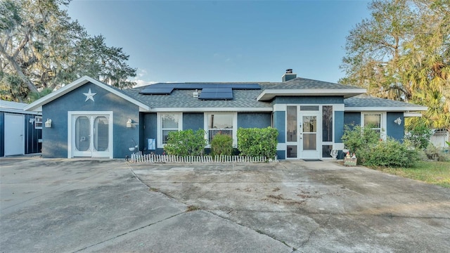 view of front of house featuring solar panels, roof with shingles, a chimney, and stucco siding