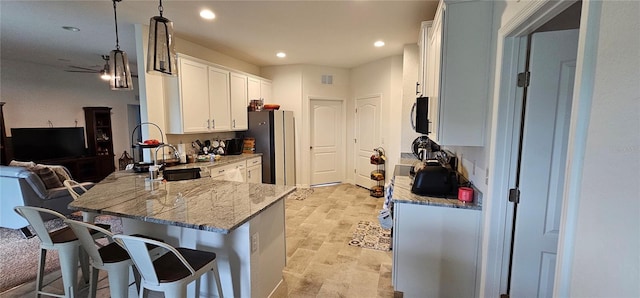 kitchen with white cabinets, a kitchen breakfast bar, freestanding refrigerator, a peninsula, and light stone countertops