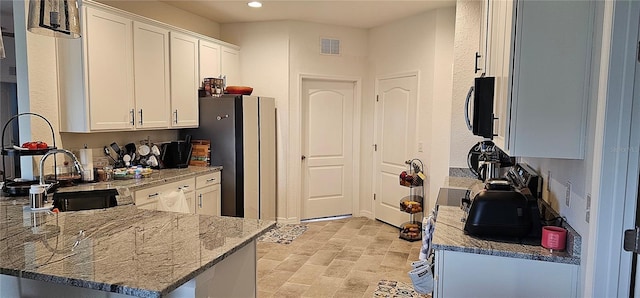 kitchen featuring stone countertops, visible vents, white cabinets, and a peninsula