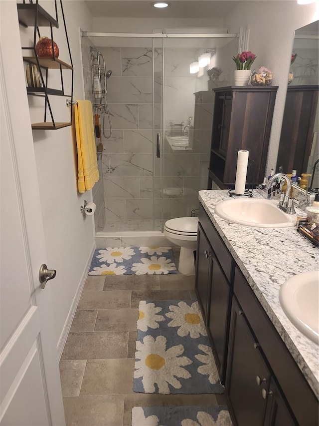 full bathroom featuring a sink, baseboards, a shower stall, double vanity, and stone tile flooring