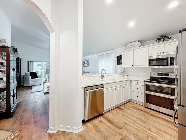 kitchen with white cabinetry, sink, stainless steel appliances, light hardwood / wood-style floors, and vaulted ceiling