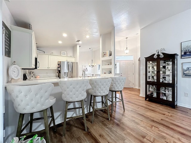 kitchen with kitchen peninsula, stainless steel fridge, pendant lighting, white cabinets, and a breakfast bar area