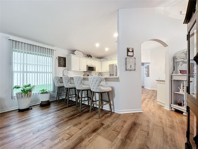 kitchen featuring white cabinetry, a kitchen breakfast bar, kitchen peninsula, lofted ceiling, and appliances with stainless steel finishes