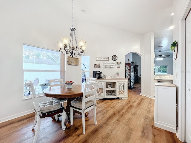 dining space with a high ceiling, light hardwood / wood-style floors, and ceiling fan with notable chandelier