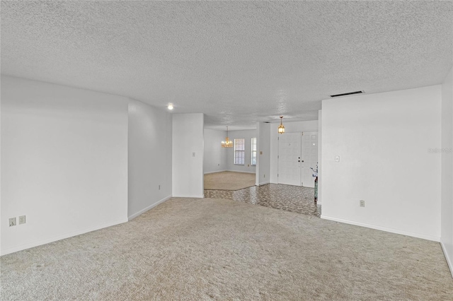 unfurnished room with a textured ceiling, carpet floors, and a chandelier