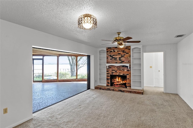 unfurnished living room featuring a brick fireplace, a textured ceiling, ceiling fan, and light colored carpet