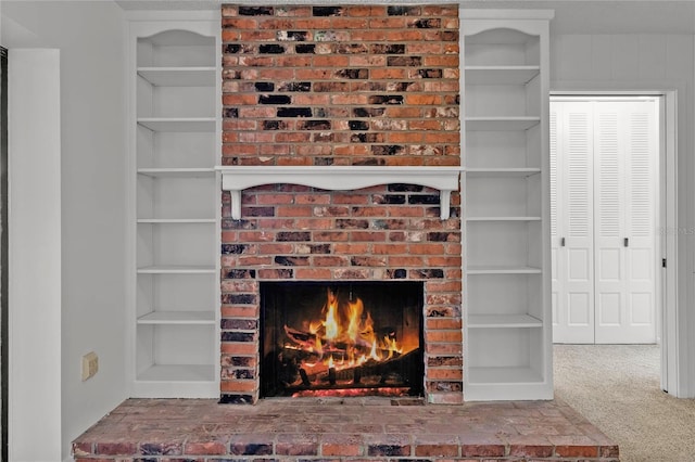 interior details featuring a brick fireplace, built in shelves, and carpet flooring