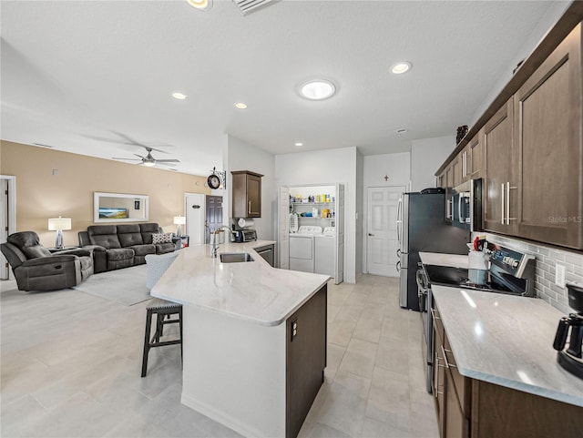 kitchen with ceiling fan, light stone countertops, a kitchen breakfast bar, separate washer and dryer, and appliances with stainless steel finishes