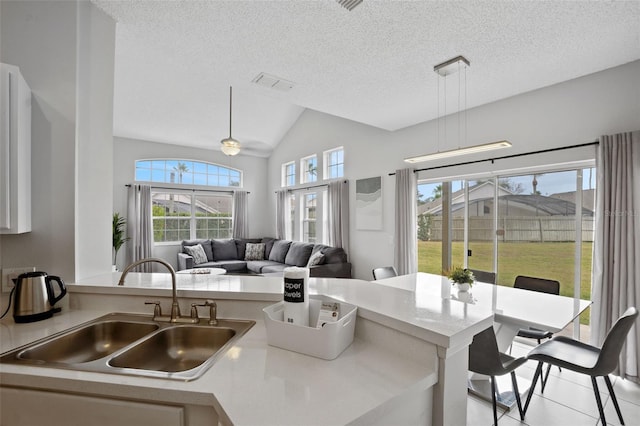 kitchen featuring pendant lighting, sink, vaulted ceiling, light tile patterned floors, and a textured ceiling