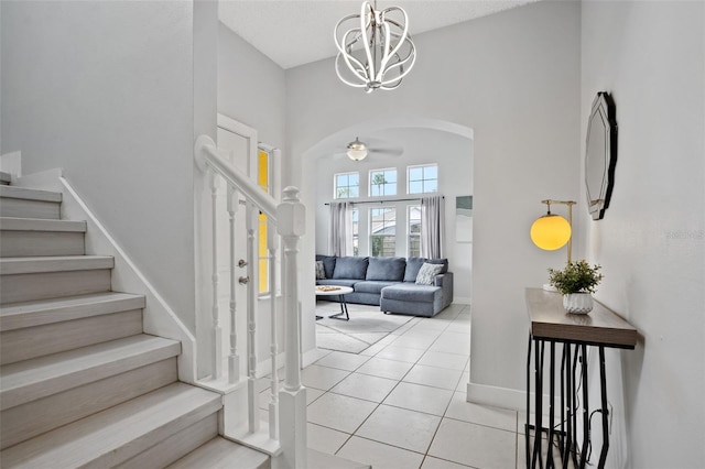 foyer with ceiling fan with notable chandelier, light tile patterned floors, and a high ceiling