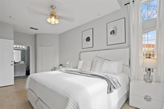 bedroom featuring ensuite bath, ceiling fan, a closet, and light wood-type flooring