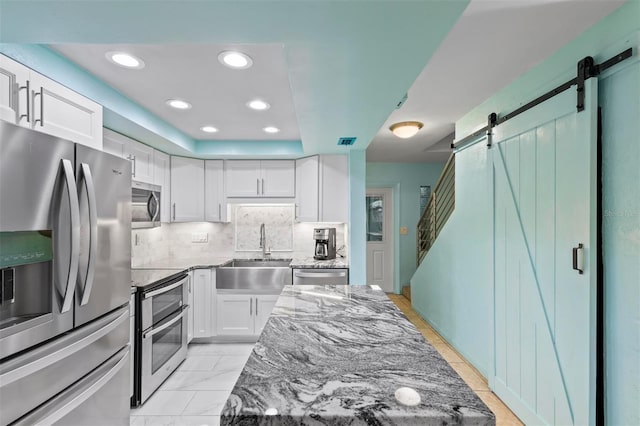 kitchen with sink, a barn door, dark stone counters, white cabinets, and appliances with stainless steel finishes