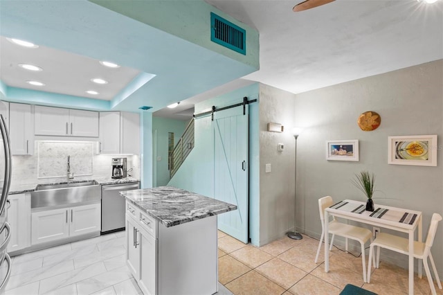 kitchen featuring white cabinetry, dishwasher, sink, a barn door, and decorative backsplash