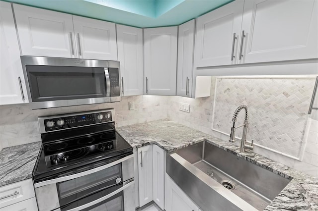 kitchen with black range with electric stovetop, sink, light stone countertops, tasteful backsplash, and white cabinetry