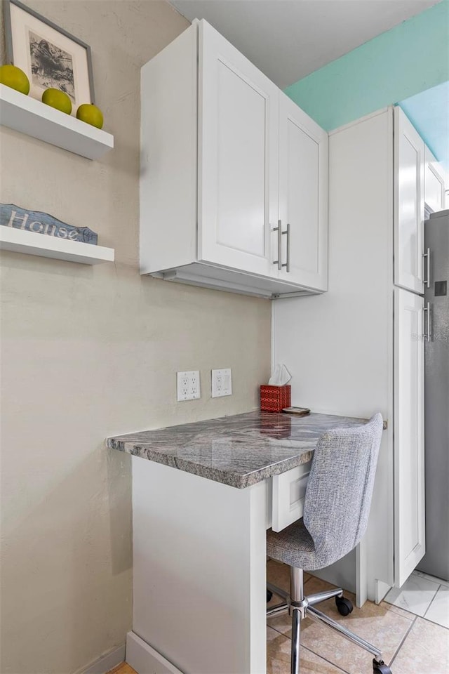 kitchen featuring stainless steel refrigerator, white cabinetry, light tile patterned floors, and dark stone counters