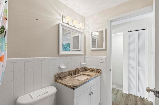 bathroom featuring wood-type flooring, vanity, toilet, and tile walls