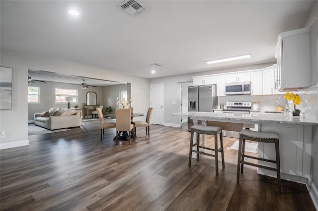 interior space with a breakfast bar area, appliances with stainless steel finishes, light stone countertops, white cabinets, and sink