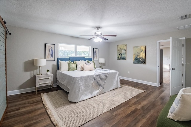 bedroom featuring a textured ceiling, ceiling fan, a barn door, and dark hardwood / wood-style floors