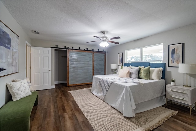 bedroom with ceiling fan, a barn door, dark hardwood / wood-style flooring, and a textured ceiling