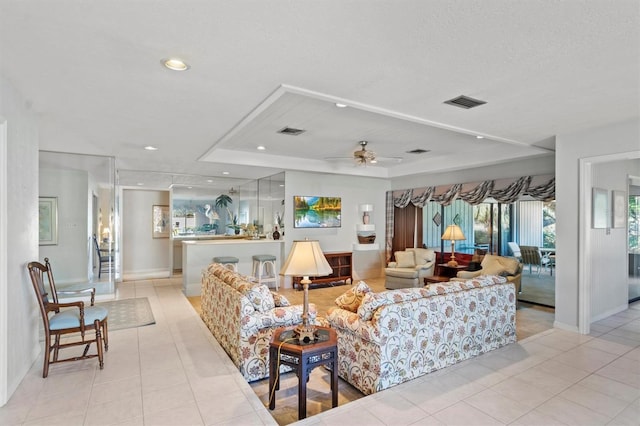 tiled living room with a tray ceiling and ceiling fan