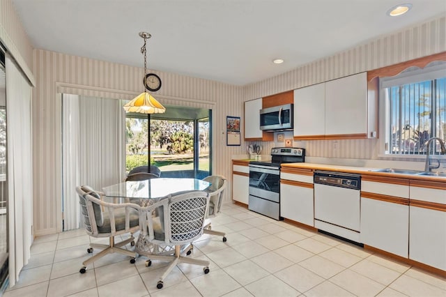 kitchen with white cabinetry, sink, hanging light fixtures, stainless steel appliances, and light tile patterned floors