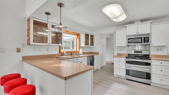 kitchen with sink, hanging light fixtures, kitchen peninsula, white cabinets, and appliances with stainless steel finishes